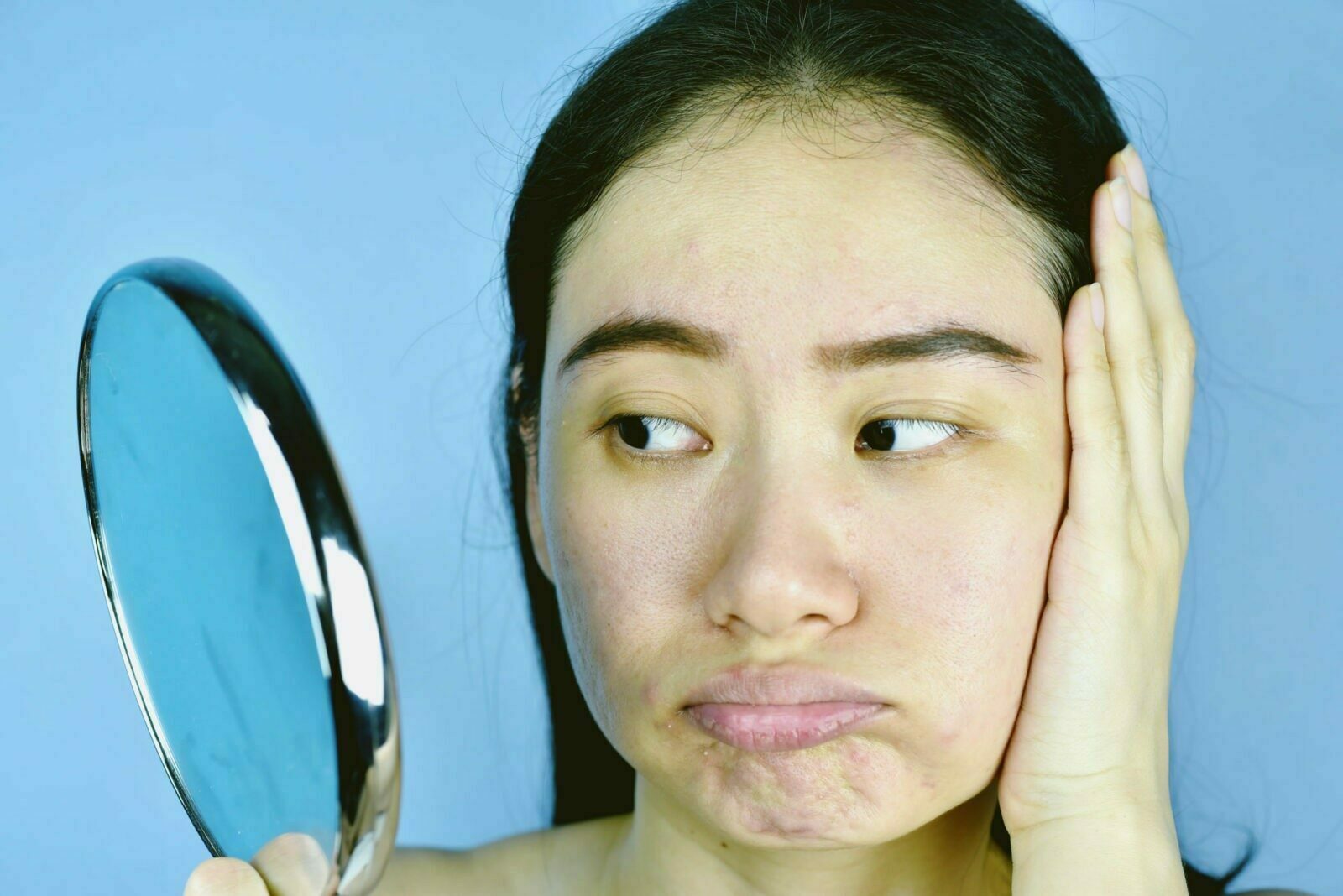 女性手拿鏡子嘟嘴煩惱皮膚老化原因